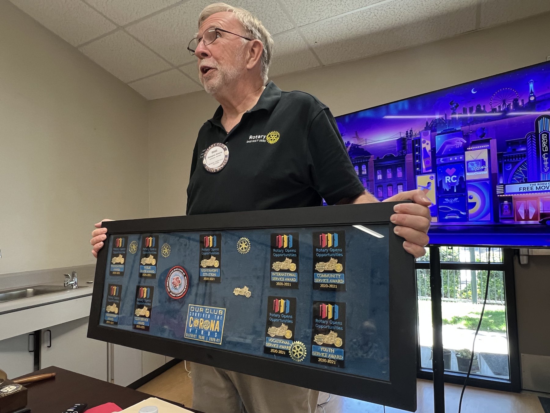 President Doug Emery holds the club's District 5330 recognition badges beside the Rotary podium