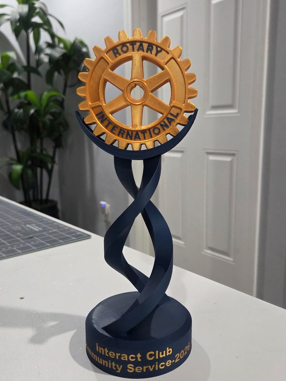 A navy and gold trophy: a Rotary International wheel mounted above a twisted double-helix column on a round base reading Interact Club Community Service 2026