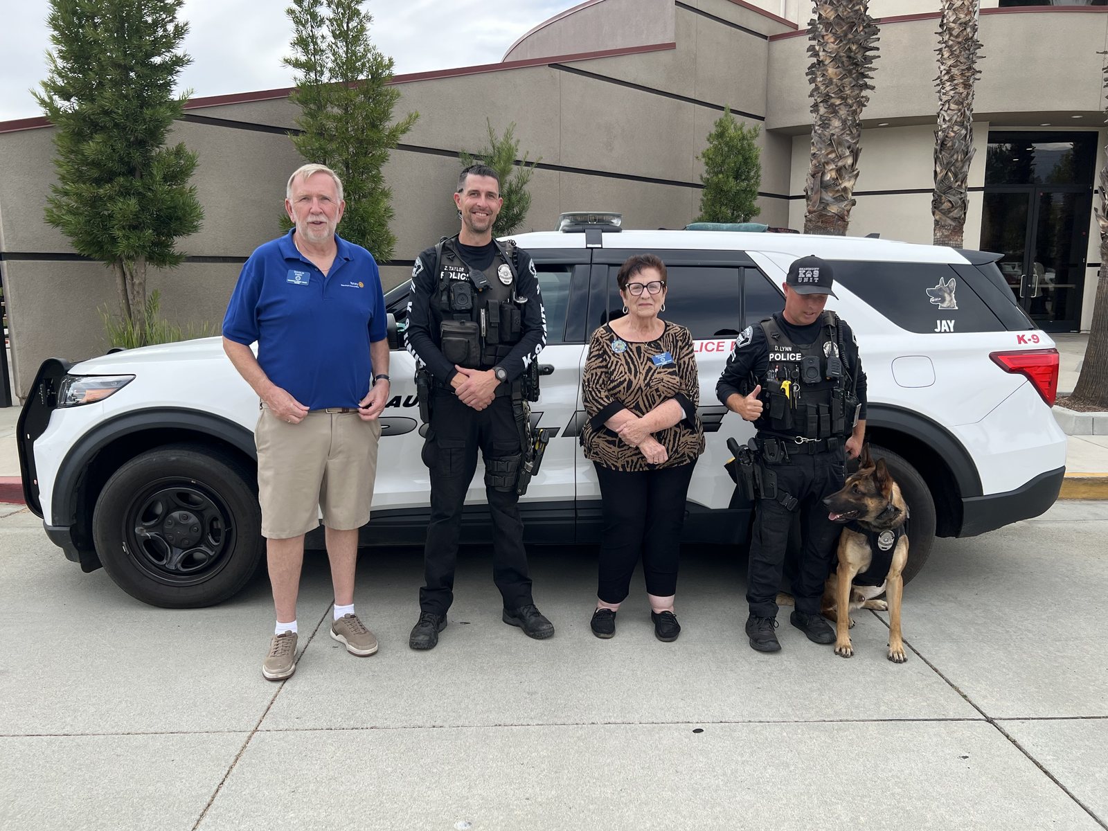 President Doug Emery and Della Condon stand with two Beaumont Police corporals and a police dog in front of a Beaumont PD K-9 unit SUV lettered Jay