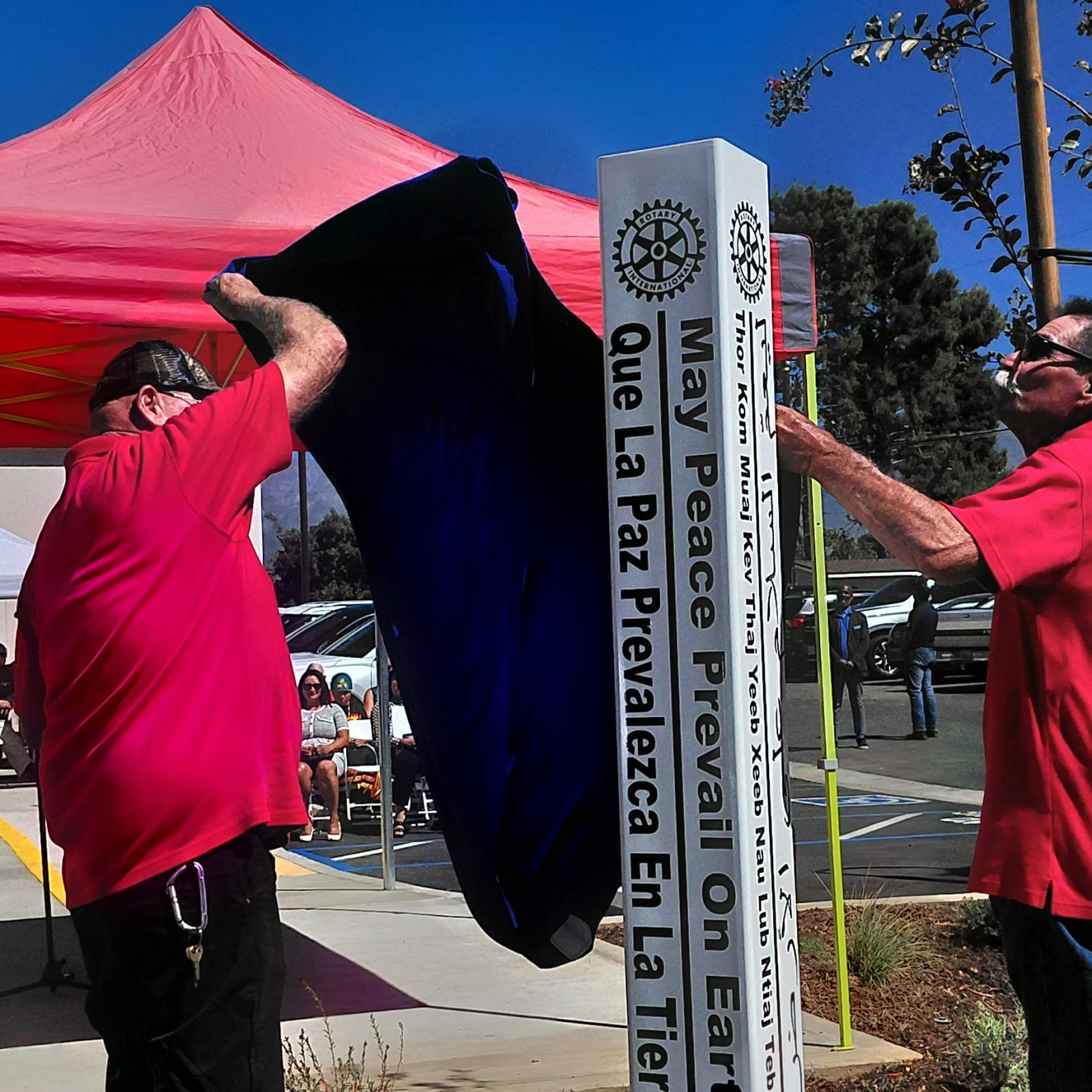 Two Rotarians pull the cover off Beaumont's second Peace Pole outside the Beaumont Library; its faces read May Peace Prevail On Earth and Que La Paz Prevalezca En La Tierra